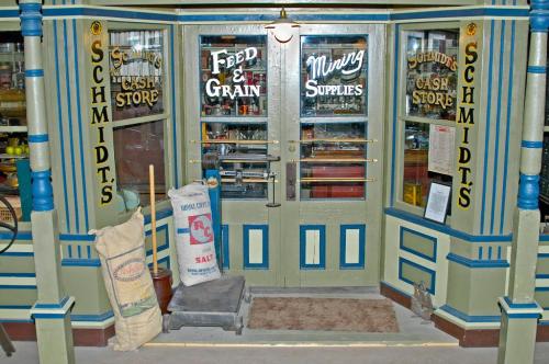 Front entrance of a vintage store labeled "Schmidt's Feed & Grain" with mining supplies, featuring wooden doors and decorative signage.
