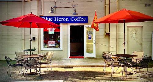 Exterior of Blue Heron Coffee with red umbrellas over tables and an open door inviting customers.