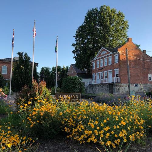 A vibrant flower bed in front of a historic building with flags and trees under a clear blue sky.