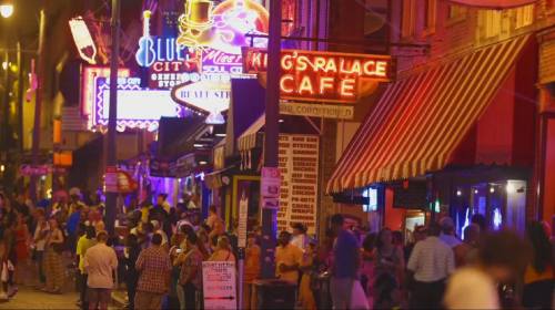 A vibrant street scene at night, filled with neon signs and crowds enjoying cafes and entertainment.