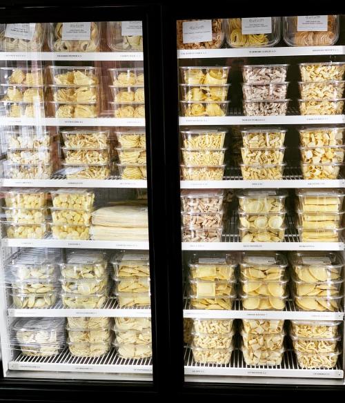 A display of various pasta types in clear containers, organized neatly in a refrigerated case.
