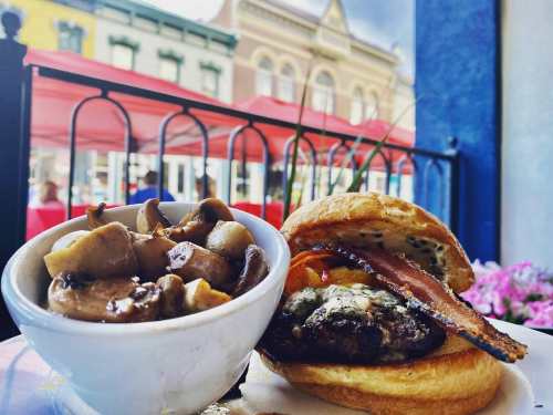 A close-up of a burger with bacon and cheese, served with a side of sautéed mushrooms on a plate.