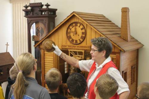 A guide shows a wooden clock and model house to a group of children during a museum tour.
