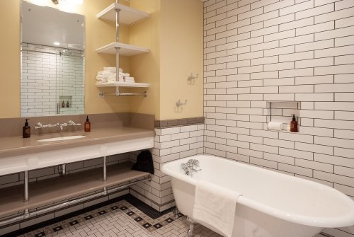 A modern bathroom featuring a freestanding tub, tiled walls, a mirror, and neatly arranged towels on shelves.