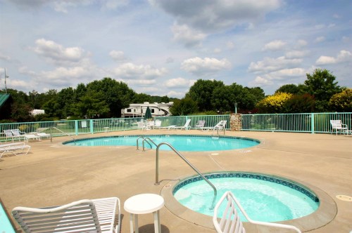 A serene outdoor pool area with a hot tub, surrounded by greenery and a cloudy sky.