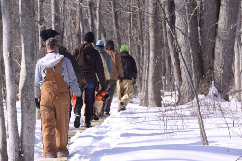 A group of people walking along a snowy forest path, surrounded by bare trees.