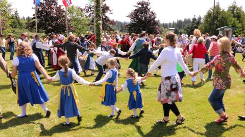 A lively outdoor scene of people dancing in a circle, wearing traditional costumes, on a sunny day.