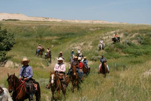 A group of horseback riders traverses a grassy landscape under a clear sky.