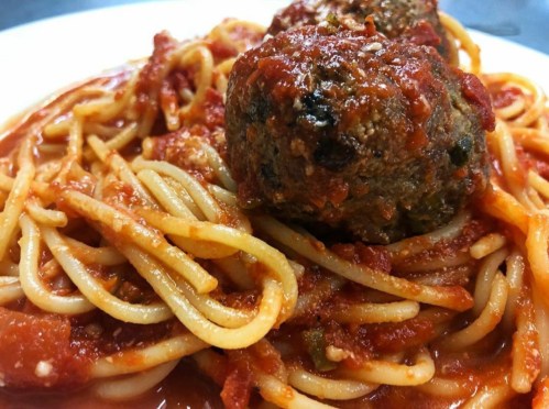 A close-up of spaghetti topped with meatballs and marinara sauce on a white plate.
