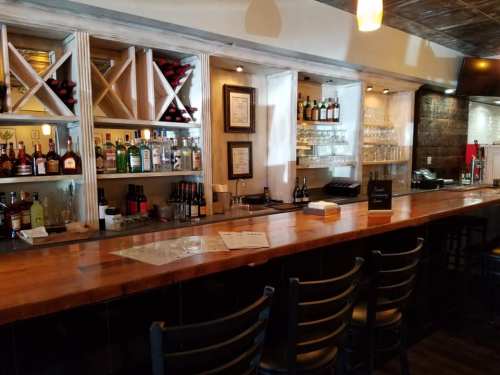 A well-lit bar with a wooden counter, shelves of liquor, and glasses, creating a cozy atmosphere.
