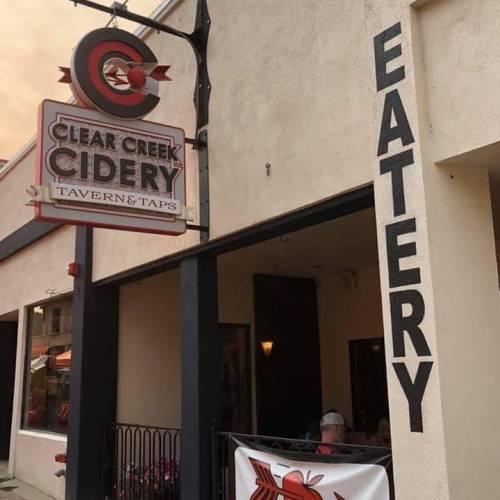 Sign for Clear Creek Cidery Tavern & Taps, featuring "EATERY" on the wall, with a cozy entrance visible.