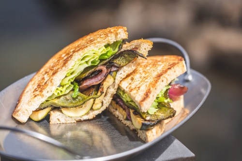 A close-up of a sandwich with grilled vegetables, lettuce, and whole grain bread, served on a metal tray.