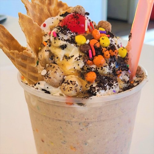 A colorful ice cream sundae topped with whipped cream, a cherry, sprinkles, and cookie crumbles in a clear cup.