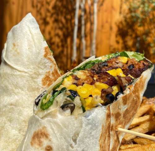 A close-up of a burrito filled with rice, beans, corn, and greens, with fries in the background.