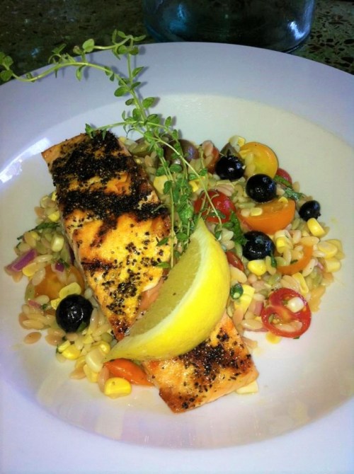 Grilled salmon fillets on a bed of colorful orzo salad, garnished with lemon and fresh herbs.