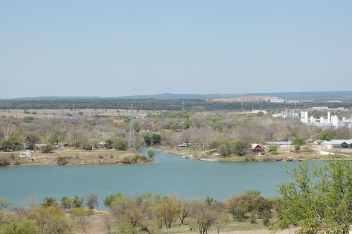 A scenic view of a river winding through green landscapes and trees, with distant hills and buildings in the background.