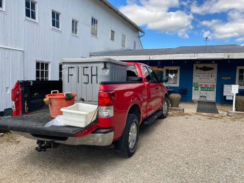 A red pickup truck parked outside a building, with containers labeled "FISH" in the truck bed.