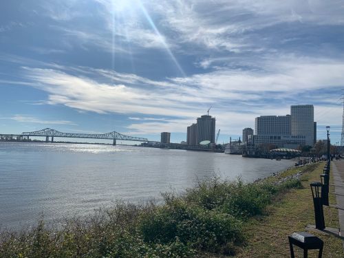 A riverfront view featuring a bridge, city skyline, and bright blue sky with scattered clouds.