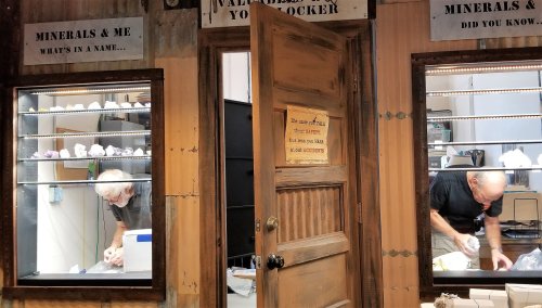 Two men examining minerals inside a shop, with signs about minerals displayed above them.