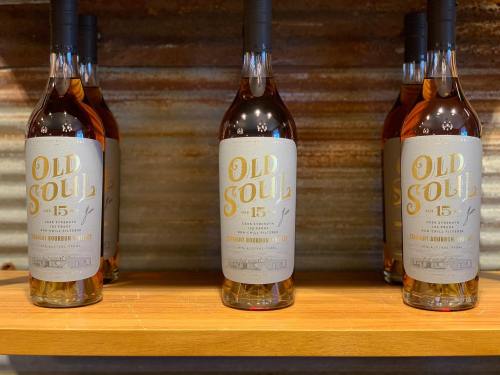 Bottles of Old Soul bourbon whiskey displayed on a wooden shelf against a rustic background.