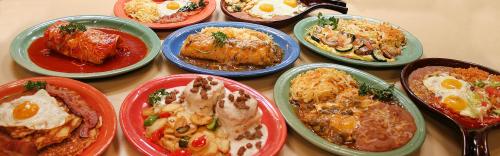 A colorful spread of various dishes, including enchiladas, rice, eggs, and vegetables, served on vibrant plates.