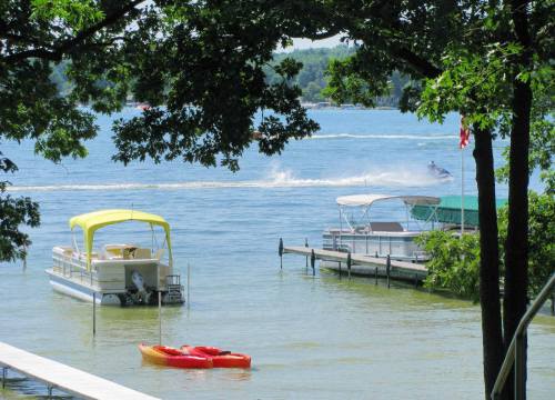 A serene lake scene with boats, kayaks, and trees, featuring a person on a jet ski in the background.