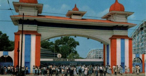 A colorful entrance gate to Riverview Park, with a crowd of people waiting outside on a sunny day.