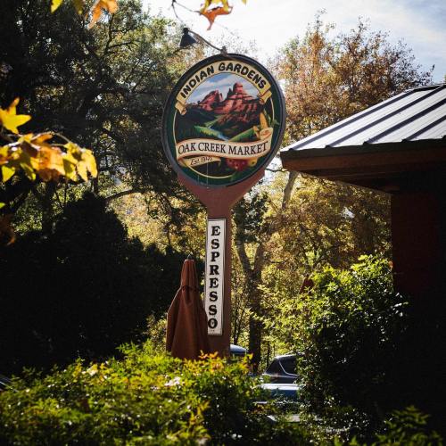 Sign for Indian Gardens Oak Creek Market with a coffee shop, surrounded by trees and autumn foliage.