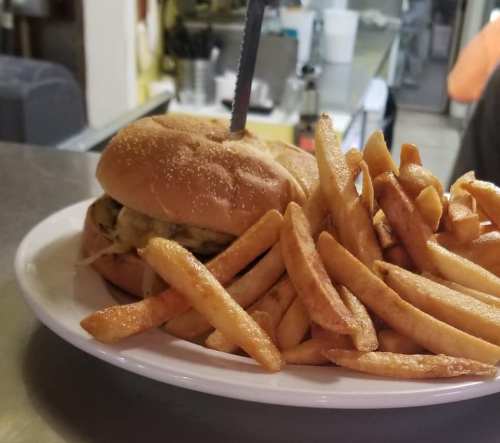 A plate with a burger topped with a skewer and a side of golden, crispy French fries.