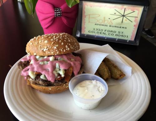 A sesame seed burger with pink sauce, lettuce, and a side of crispy fries on a plate, with a restaurant sign in the background.