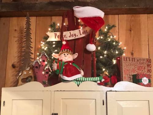 A festive display with an elf, Christmas lights, a Santa hat, and holiday decorations on a wooden shelf.