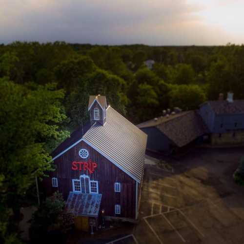 Aerial view of a rustic barn with a red "STRIP" sign, surrounded by trees and a parking area.