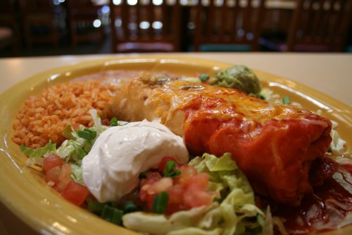 A plate of Mexican food featuring a burrito, rice, guacamole, sour cream, and a fresh salad.