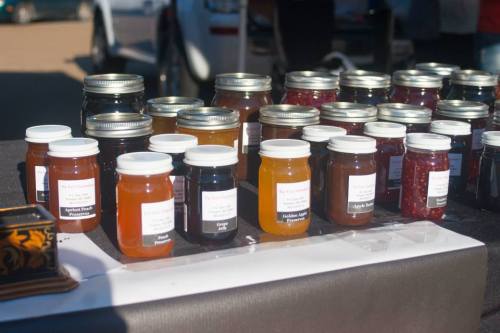 A display of various jars of preserves and jams on a table at a market, labeled with different fruit flavors.