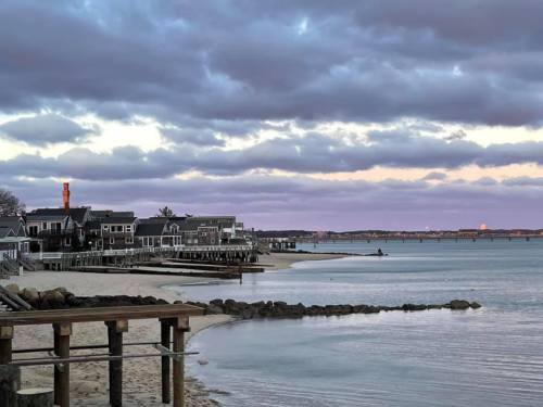 A serene waterfront scene with houses along the shore, calm water, and a cloudy sky at dusk.