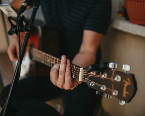 A close-up of a person playing an acoustic guitar, focusing on their hand and the instrument's neck.