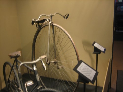 A vintage bicycle display featuring a high-wheel penny-farthing and a modern bike, with informational plaques.