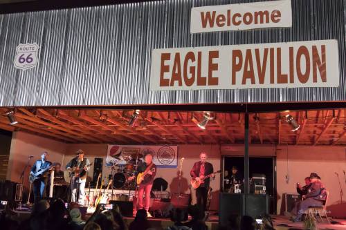 A live band performs on stage at Eagle Pavilion, with a "Welcome" sign and audience in front.