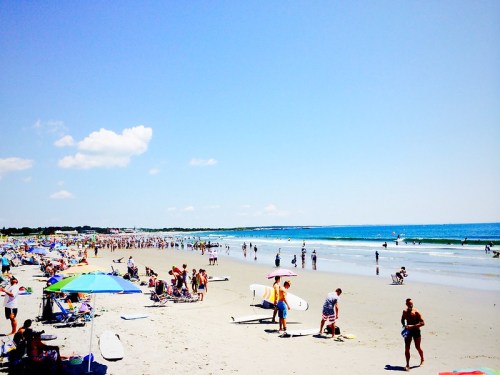 A sunny beach scene with people enjoying the water, colorful umbrellas, and a clear blue sky.