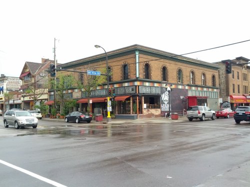A street view of a historic building with colorful awnings, surrounded by cars and trees on a rainy day.