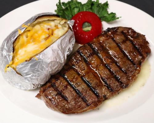 A grilled steak with grill marks, served alongside a baked potato topped with cheese and a slice of tomato.