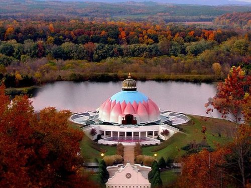 A colorful lotus-shaped building surrounded by autumn trees and a serene lake.