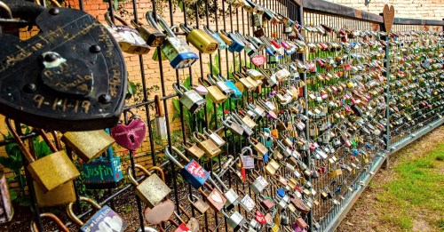 A fence covered in colorful padlocks, symbolizing love and commitment, set against a brick wall.