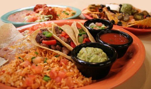 A colorful spread of tacos, rice, guacamole, salsa, and nachos on vibrant plates.
