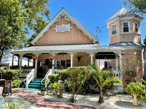 A charming pink building with white trim, surrounded by greenery, featuring a tower and a welcoming porch.