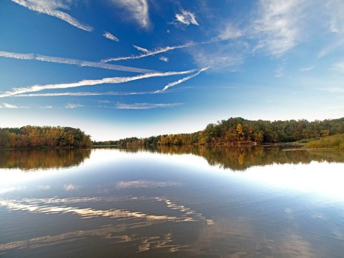 A serene lake reflects a clear blue sky with wispy clouds and colorful trees along the shore.