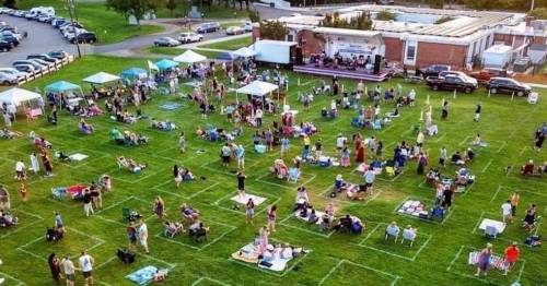 Aerial view of a large outdoor gathering with tents and people sitting on the grass, enjoying a community event.
