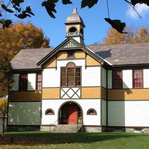 Historic building with a bell tower, colorful exterior, and large windows, surrounded by autumn foliage.