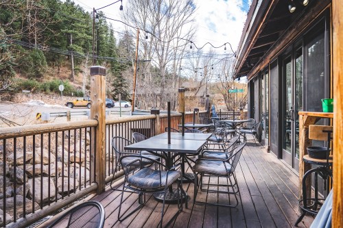 A wooden deck with tables and chairs, surrounded by trees and a view of a road in a mountainous area.