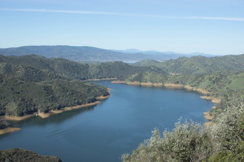 A serene lake surrounded by lush green hills under a clear blue sky.